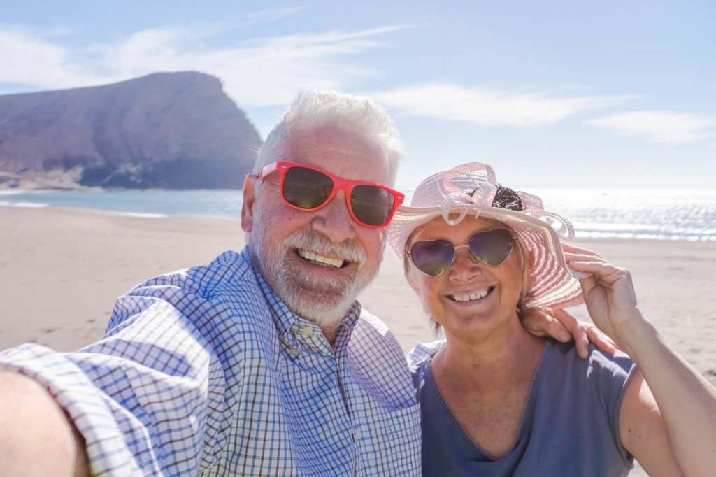 couple of seniors traveling and taking a selfie in a beautiful beach with a mountain